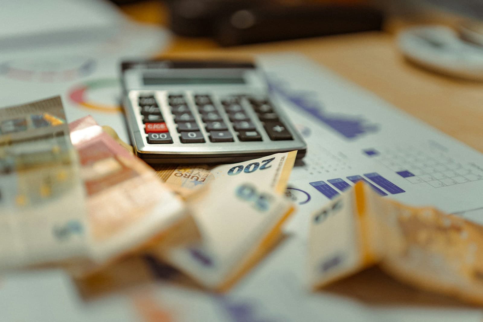 Une calculatrice posée sur des billets et des tickets de caisse, sur un plan de travail clair.