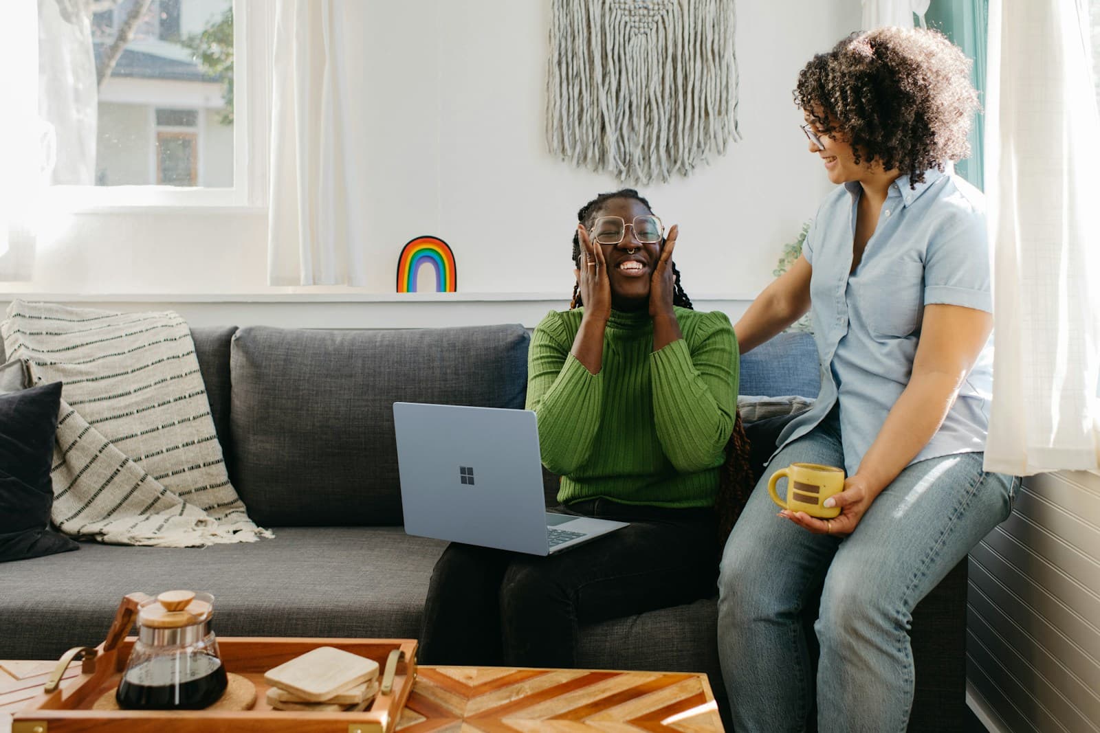 Une femme assise sur un canapé, un téléphone à l'oreille, un ordinateur portable posé devant elle.